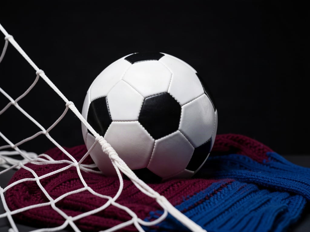 Minge de fotbal, plasă și eșarfă vișinie-albastră într-o compoziție editorială despre derby-ul FCSB – Rapid